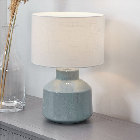 Nora Duck Egg Blue Crackle Effect Table Lamp, 44cm, with a rounded ceramic base and white drum shade, shown on a grey sideboard beside a glass vase.