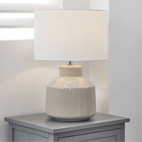 Nora Cream Crackle Effect Table Lamp, 44cm, with a ceramic crackle-glaze base and white linen drum shade, shown on a grey bedside cabinet.