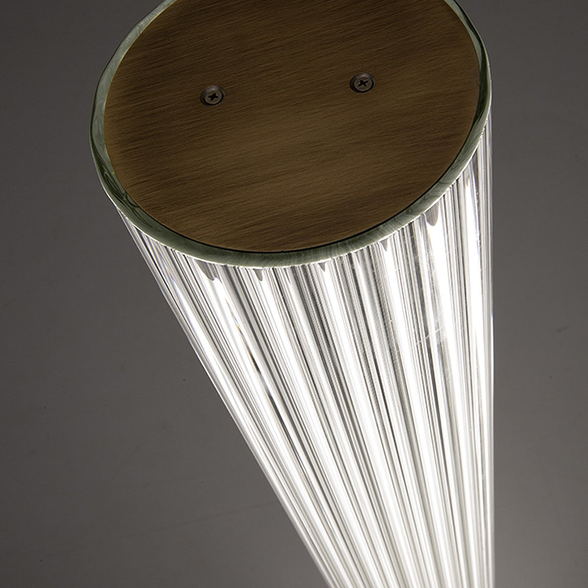 Close-up of the Dalvorne glass floor lamp's satin bronze top cap with visible screws, sitting atop ribbed glass column illuminated from within.