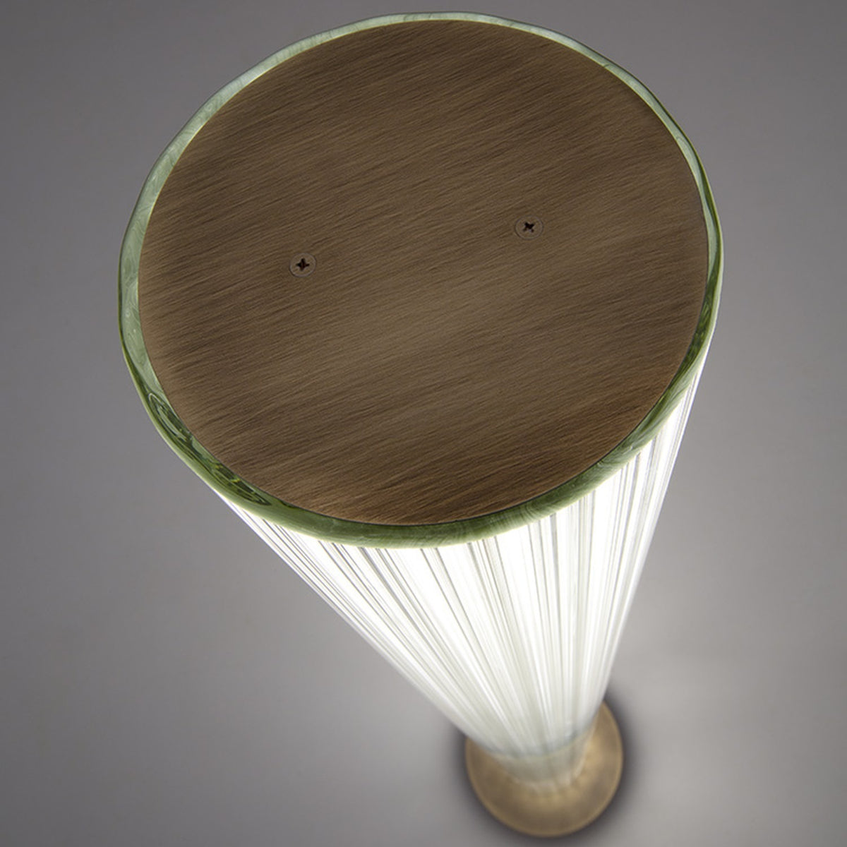 Top-down view of the Dalvorne glass floor lamp showing its round satin bronze cap with visible screws above the illuminated ribbed glass column.