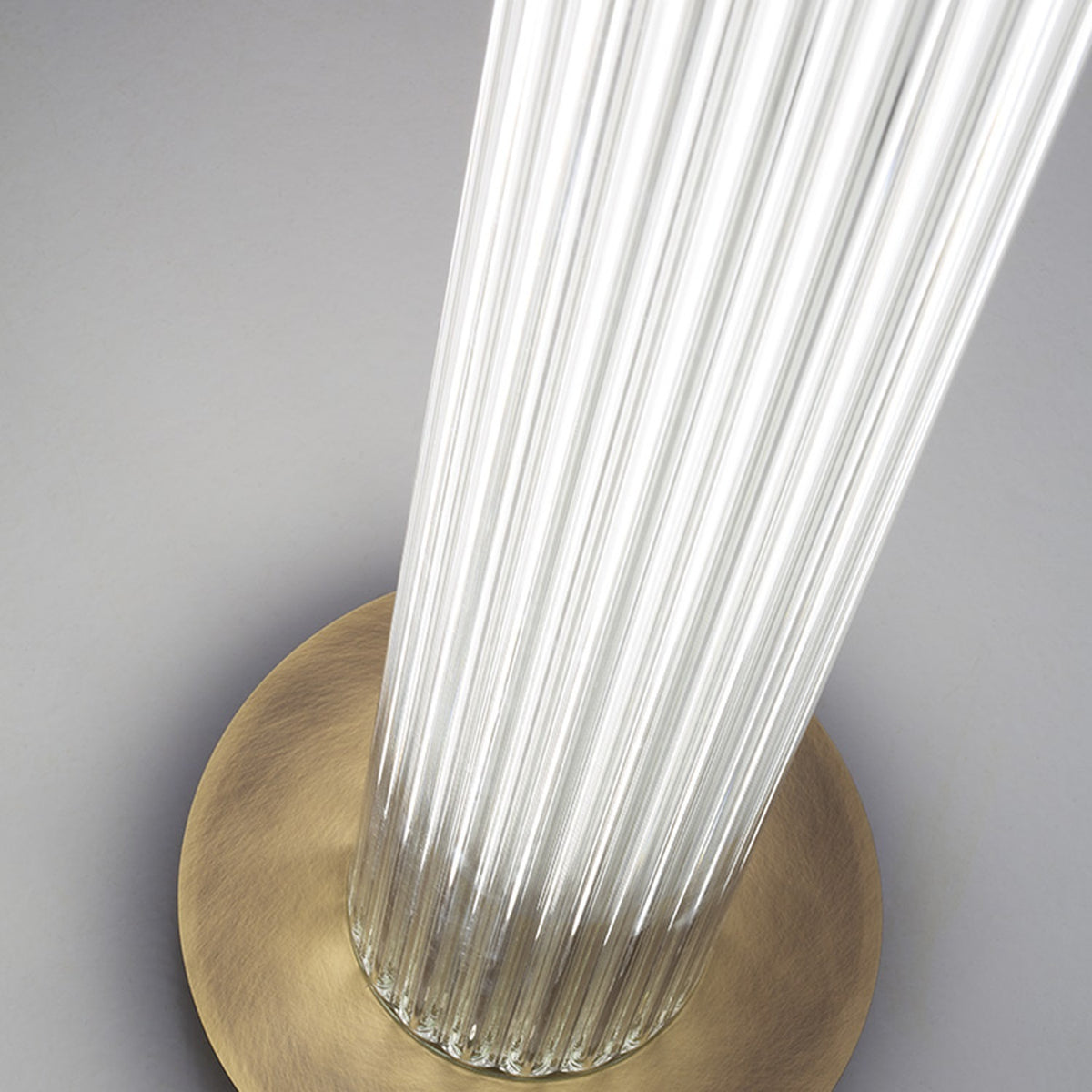 Close-up of the Dalvorne Glass Floor Lamp's satin bronze round base, where ribbed glass column meets the finish against a plain grey background.