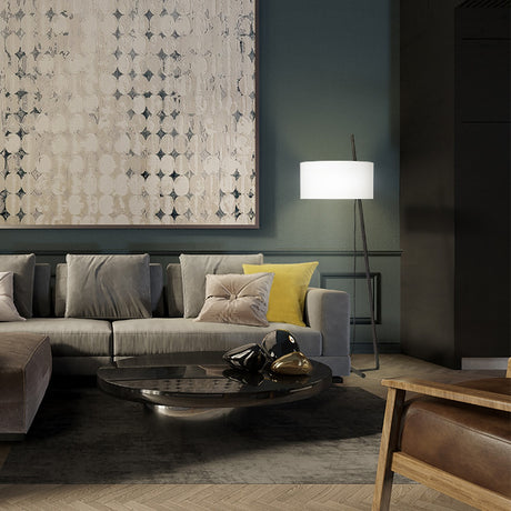 Gilvorne fabric floor lamp with slanted anthracite iron stem and white cotton drum shade, shown beside a grey sofa in a living room setting.