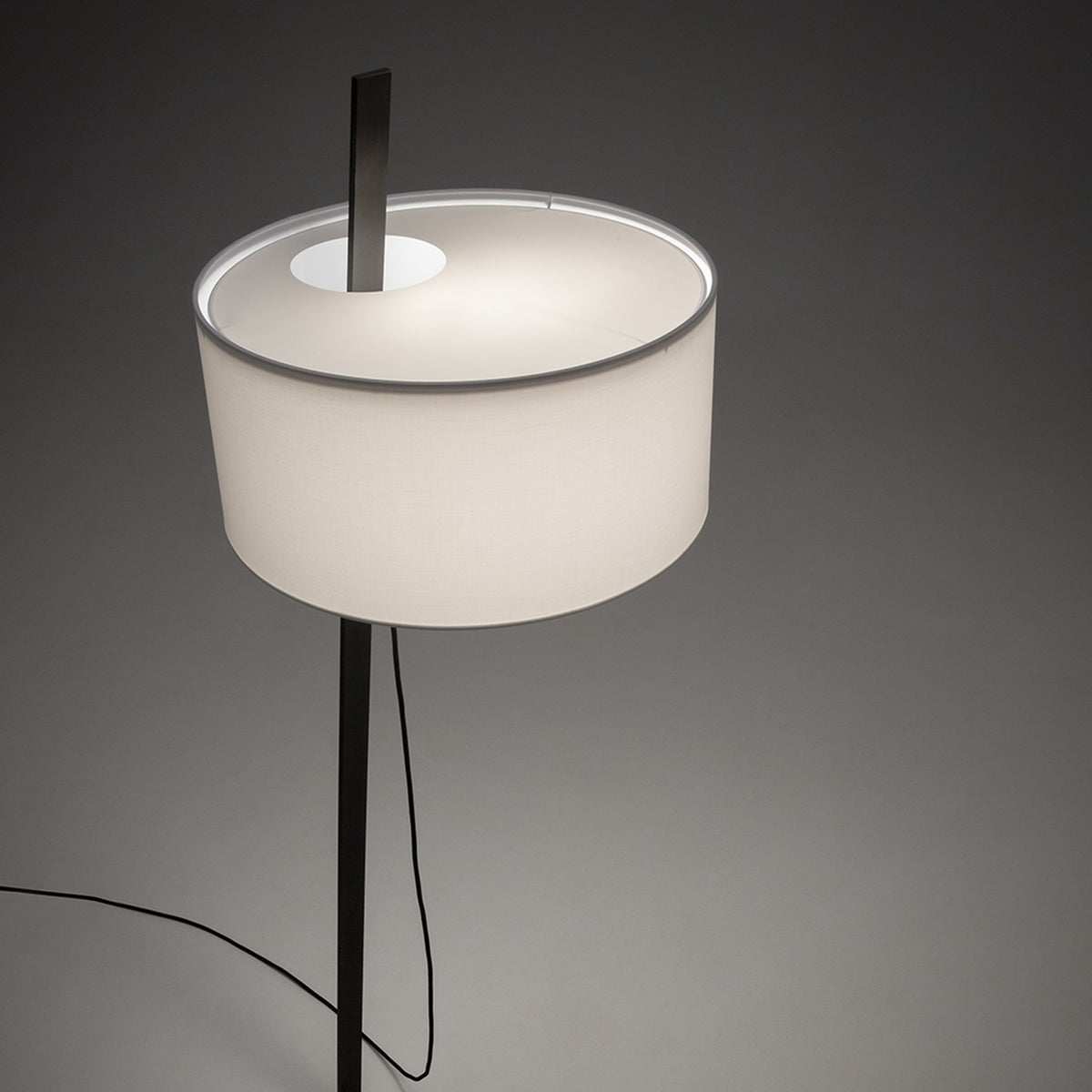 Gilvorne Fabric Floor Lamp with slim anthracite iron stem and broad white cotton drum shade, glowing softly against a plain grey background.