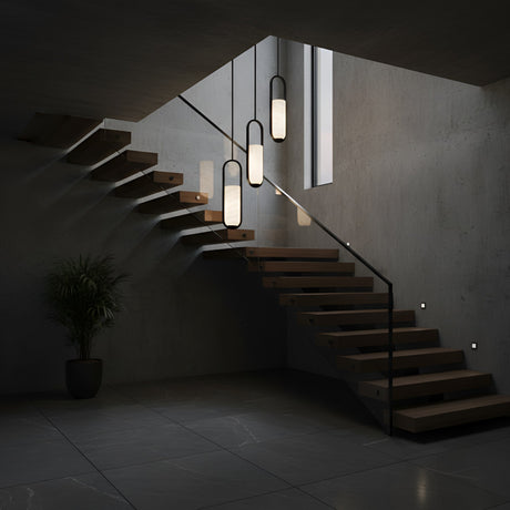 Modern floating wooden staircase with matte black railing, concrete walls and floor, a tall window, a potted plant in the corner, and the Arvion 1 Light Slim Capsule Alabaster Single Pendant Light in Soft White & Matte Black.