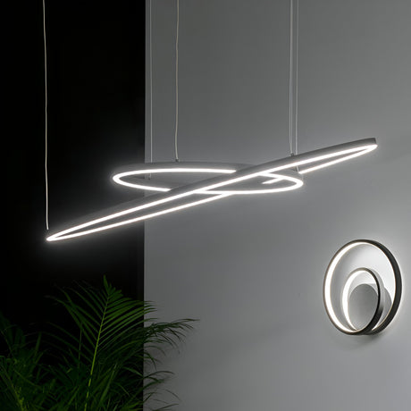 An Arcena Round LED Suspension Light, featuring a modern and sculptural design with glowing rings, hangs from the ceiling in a dimly lit room. Nearby, a similar circular wall light with warm white LEDs is mounted on a gray wall. Green plants are partially visible in the foreground.