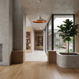 A modern, minimalist interior with light wood floors, concrete walls, large windows, built-in planters of greenery, shelves displaying decor, and a Funk Wide Pendant Light - White. Ample natural light brightens the open space.
