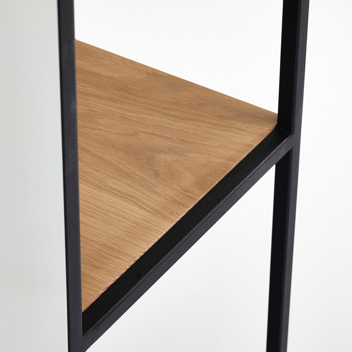 Close-up of the Chassis XL free standing mirror's black metal frame with a solid oak shelf set horizontally inside, shown against a plain white background.