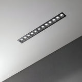 A contemporary, rectangular recessed light fixture integrated into a gray ceiling showcases the energy-saving Phosix Slim LED Recessed Downlight. With its sleek design, this 20W, 3000K black fixture features multiple round bulbs that emit a gentle glow, highlighting the ceiling's smooth, textured finish.