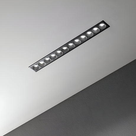 A contemporary, rectangular recessed light fixture integrated into a gray ceiling showcases the energy-saving Phosix Slim LED Recessed Downlight. With its sleek design, this 20W, 3000K black fixture features multiple round bulbs that emit a gentle glow, highlighting the ceiling's smooth, textured finish.