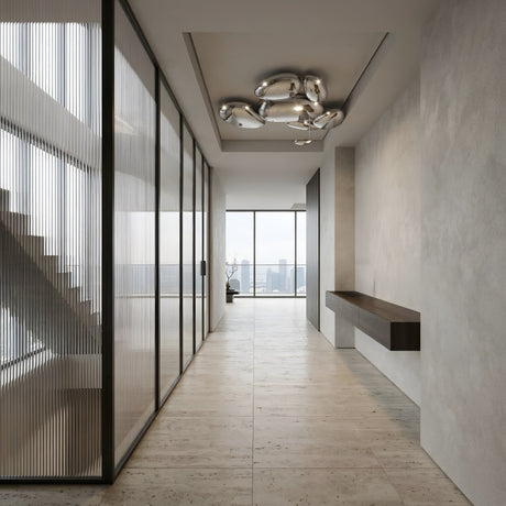 Niori Skydro LED Flush Ceiling Light in polished silver, its chrome pebble cluster mounted in a recessed ceiling above a hallway with city-view windows.