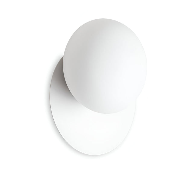 A minimalist design showcasing a white sphere intersecting with a flat circular base, reminiscent of the Halion Wall Light - White. The interplay of shapes casts a gentle shadow on a simple white background, highlighting simplicity and modernity with an ambient glow.