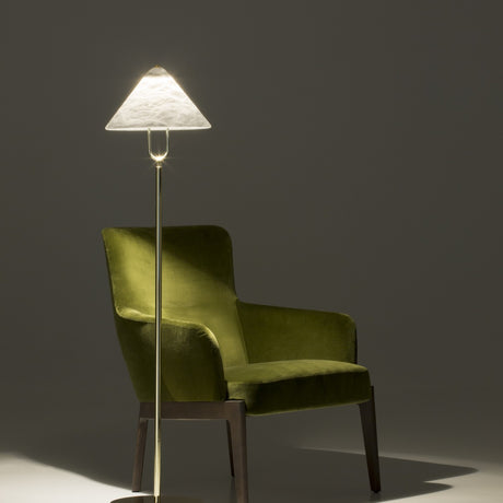 Fuji LED floor lamp with triangular alabaster shade on a polished brass stem and U-shaped yoke, shown lit beside a green velvet armchair.