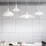 A modern, minimalistic office space is illuminated by four Arion Small Ceiling Lampshades in White, hanging gracefully from the ceiling to elevate the industrial-style interior. The background features a wall with geometric paneling, while the foreground displays a desk decorated with open books and essential office supplies.