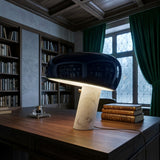 Niori Sleepy Marble Table Lamp with glossy black domed shade and white marble base on a wooden desk beside leather books in a library setting.