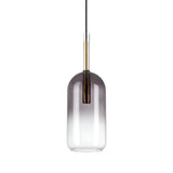 The Empire-2 1 Light Glass Pendant - Black features a cylindrical glass shade transitioning from smoky grey to clear, compatible with E27 bulbs, and is accented with brass details and a black cord, all set against a white backdrop.