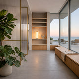 Modern living space with large windows and ocean views, featuring a Vera Dimmable LED Strip Table Lamp - Clear for soft ambient lighting, a built-in wooden bench with throw, potted plant, open shelves with decor, and minimalist airy design.