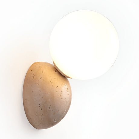 The Belaro 1 Light Globe Travertine Wall Light in light beige features a smooth white glass globe shade set on a textured oval travertine base, creating an elegant accent for any white wall.