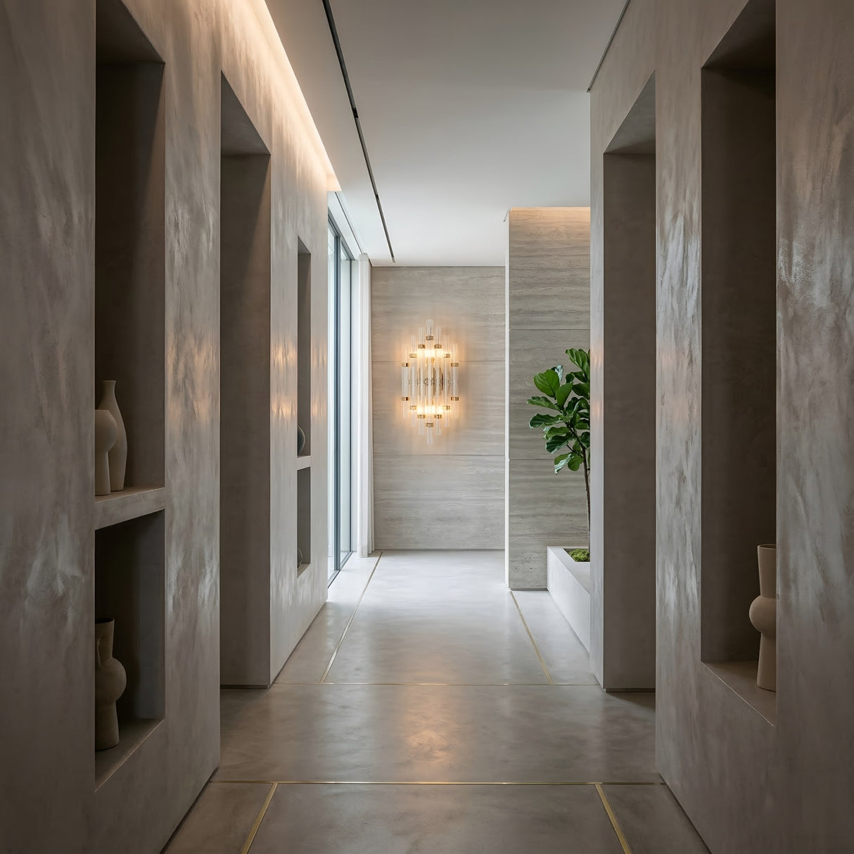 Magari 2 Light Crystal Glass Wall Light in gold illuminated at the end of a grey plaster hallway with built-in niches, vases, and a fiddle-leaf fig.