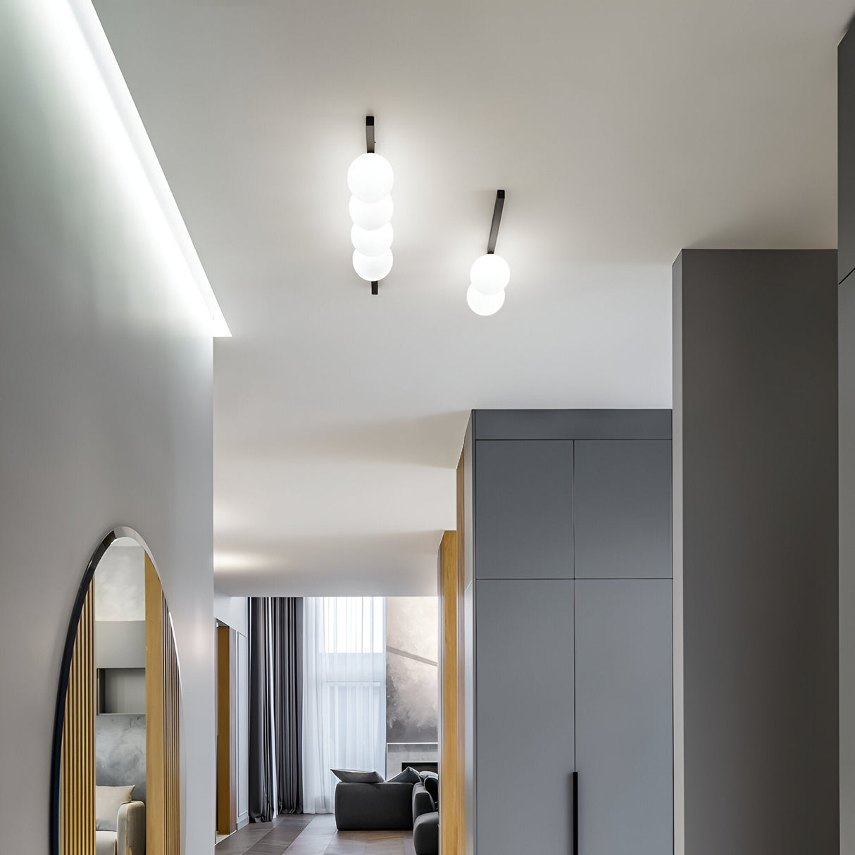 A modern interior with minimalist design features a hallway and living space. The room showcases soft, neutral colors with a large floor-standing mirror, sleek cabinets, and a Phostis 4 Light Ceiling & Wall Light in Black. Large windows with sheer curtains complete the look with a touch of elegance.