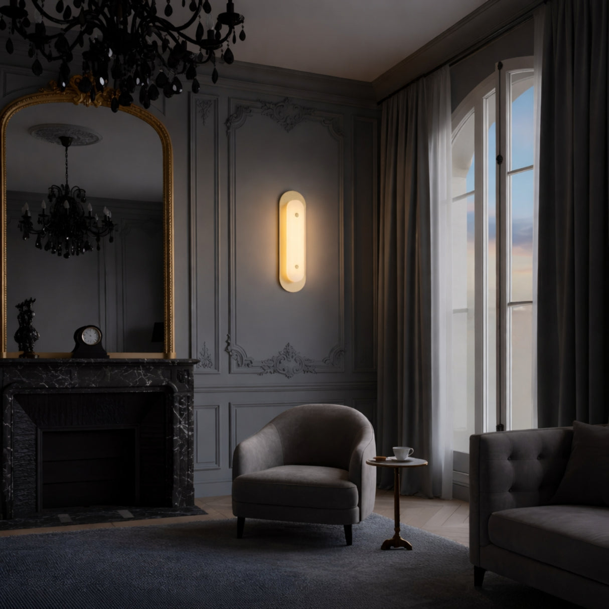 A sophisticated living room with ornate wall paneling, marble fireplace, gilded mirror, and tall curtained windows. The Avelora LED Small Capsule Alabaster Wall Light in Soft White & Brass adds modern elegance beside an armchair and gray sofa.