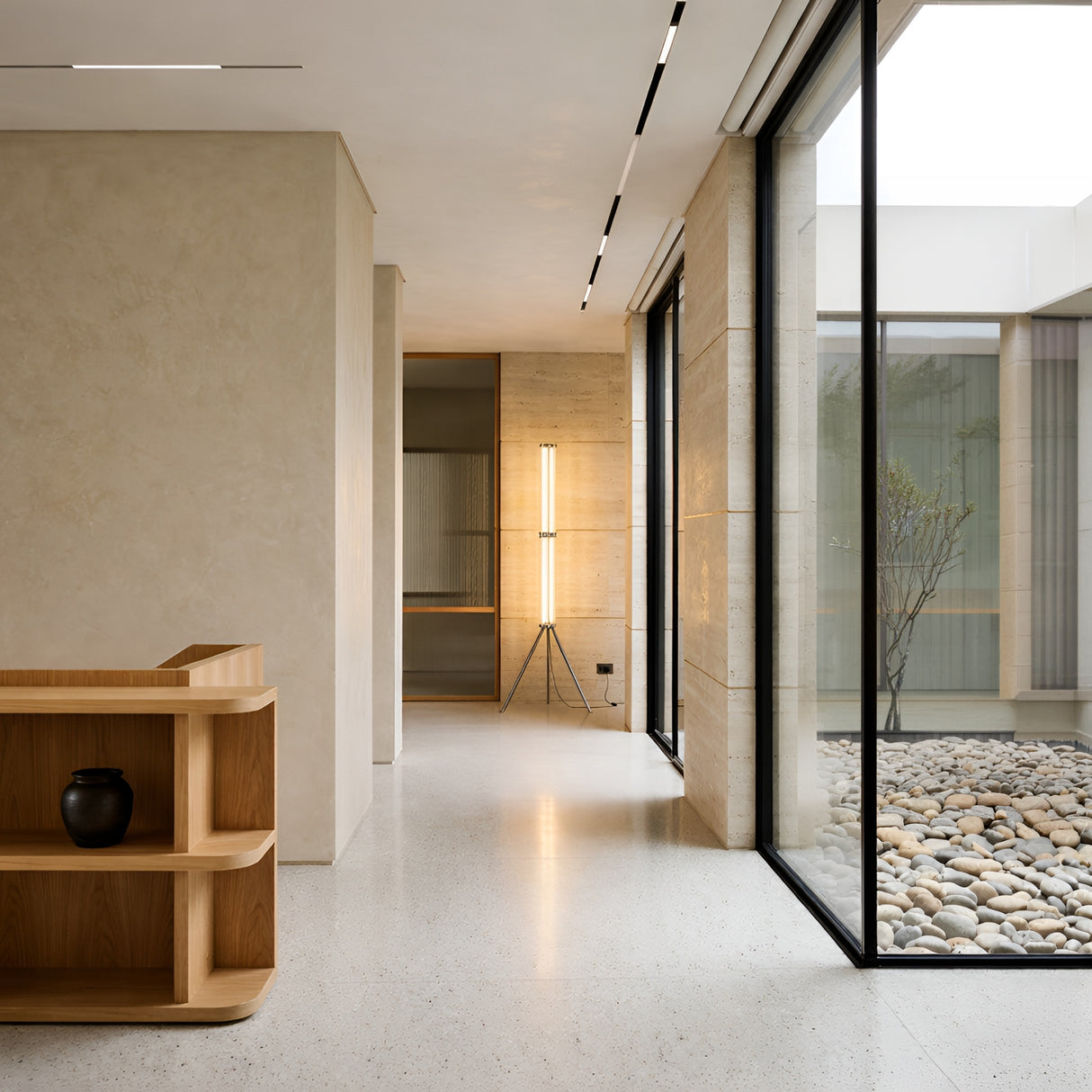 A modern minimal interior with beige walls, terrazzo floor, large glass windows facing a stone courtyard, wooden shelves with a black vase, and the Vera Dimmable LED Strip Floor Lamp - Clear illuminating the background.