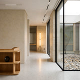 A modern minimal interior with beige walls, terrazzo floor, large glass windows facing a stone courtyard, wooden shelves with a black vase, and the Vera Dimmable LED Strip Floor Lamp - Clear illuminating the background.