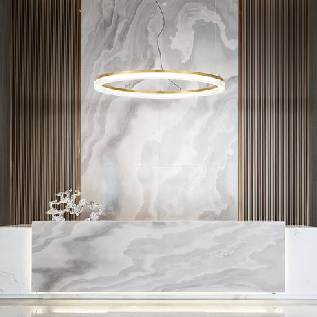 A modern reception area showcases a marble desk and wall accented by delicate gray veining. Overhead, the Soltra LED Light Suspension 30W 3000K in Brass, measuring 80cm, illuminates the space with its opal acrylic diffuser. To the left, an abstract metallic sculpture introduces a touch of elegance, while vertical panels frame the marble backdrop.