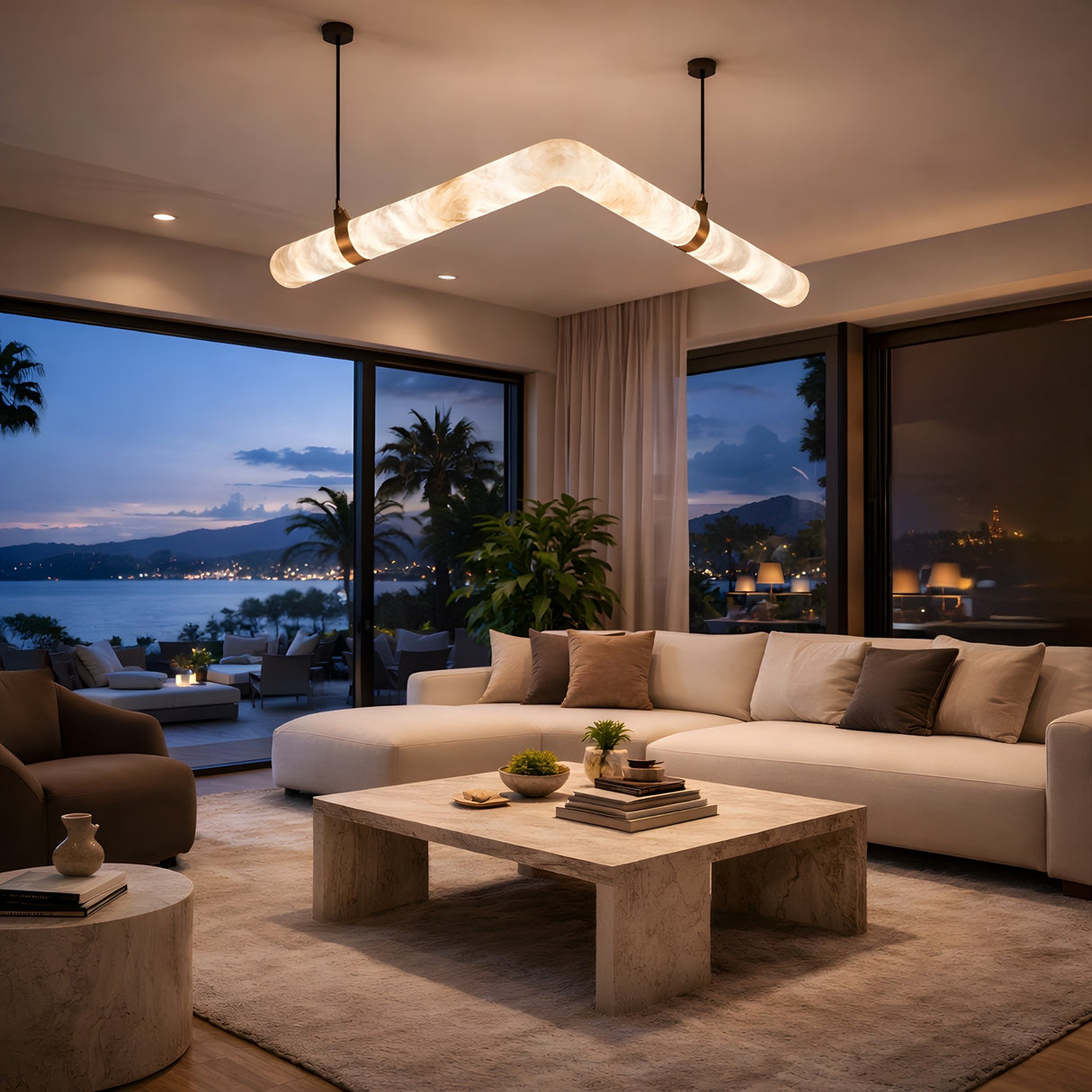 Niori Zareon chevron alabaster chandelier with brushed brass collars, illuminated above a marble coffee table and cream sofa in a coastal living room.