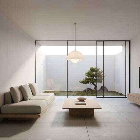 A minimalist living room features light furniture, a low wooden table, large glass doors to a bonsai courtyard, and is softly illuminated by the Elvara 1 Light Bowl Alabaster Single Pendant Light in Soft White & Brushed Brass.