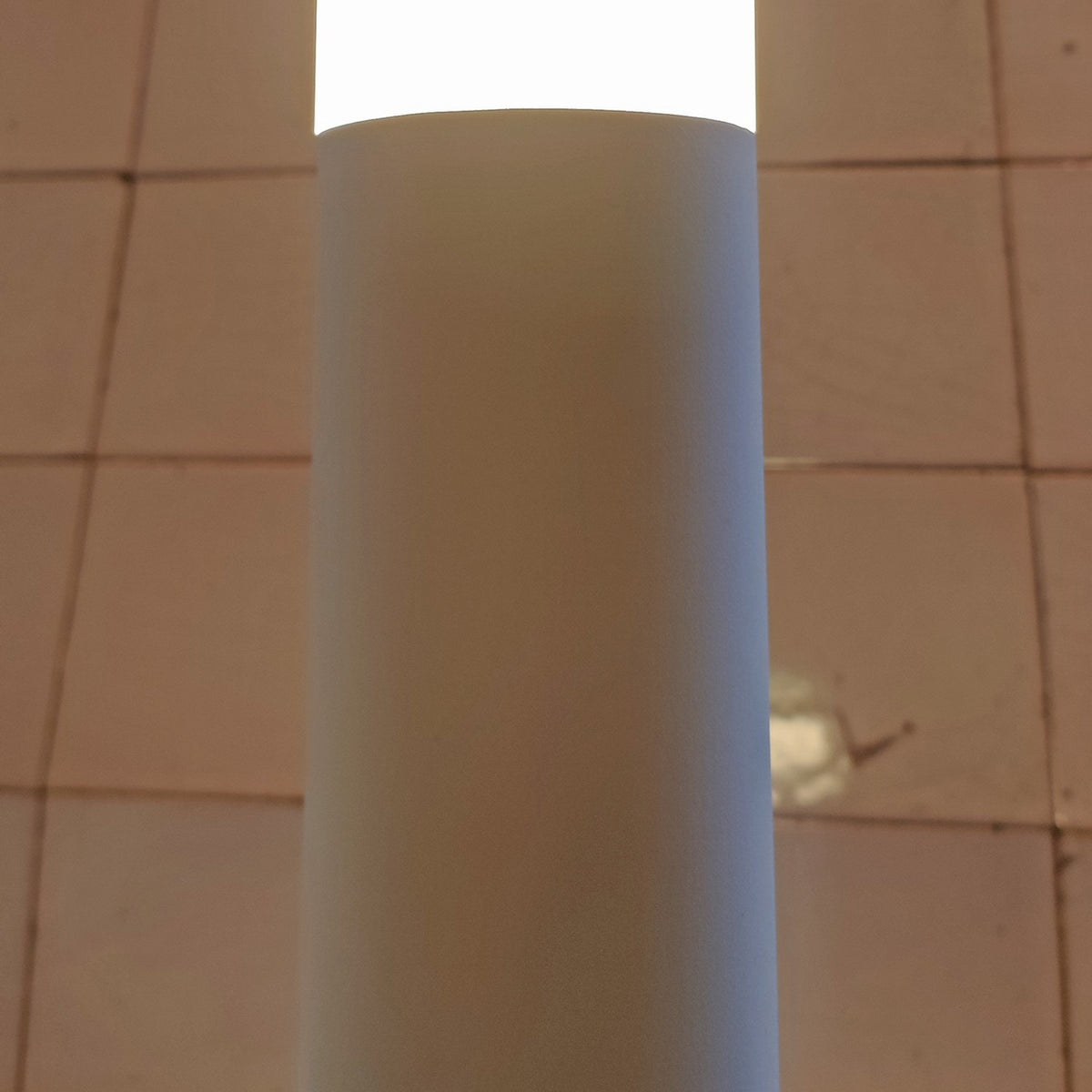 Close-up of the Wynorne LED floor lamp's textured white aluminium column and frosted acrylic diffuser, glowing warm white against a tiled wall.