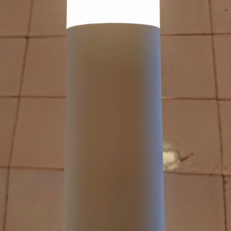 Close-up of the Wynorne LED floor lamp's textured white aluminium column and frosted acrylic diffuser, glowing warm white against a tiled wall.