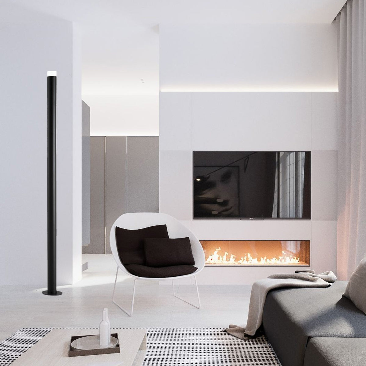Wynorne LED Floor Lamp in textured black, a tall slim aluminium column with white acrylic top diffuser, shown beside a fireplace in a modern living room.