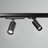 A pair of Glimmara LED Three Phase Track Spotlights, featuring a sleek black design and energy-efficient 21W power with a warm 3000K temperature, are mounted on a ceiling rail against a neutral gray background. The cylindrical heads are angled in different directions, allowing for adjustable illumination.