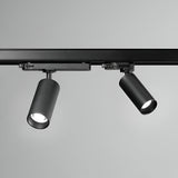A pair of Glimmara LED Three Phase Track Spotlights, each with an 8W 3000K output in black, are mounted on a ceiling rail. One energy-efficient light is angled downward while the other features an adjustable head tilted slightly to the side, illuminating a plain grey background and highlighting their sleek, cylindrical design.