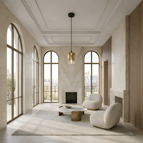 A modern, minimalist living room with large arched windows, cream walls, a marble fireplace, two rounded beige armchairs, a marble coffee table, the Slice Glass Pendant Light - Gold overhead, and city rooftops visible outside.