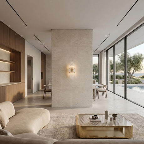 A modern, minimalist living and dining area with large windows, beige sofa, gold coffee table, marble accent wall, built-in shelves, and the Magari Crystal Wall Light in Gold & Clear Glass elevates the neutral décor and frames pool and tree views.