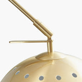 Close-up of the Feliciani floor lamp's brushed brass adjustable head and pivot joint atop a perforated globe shade, shown against a plain white background.