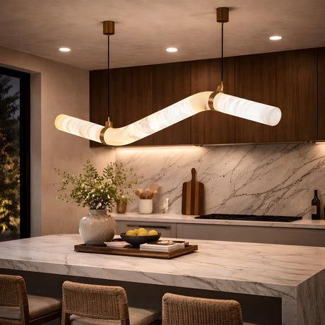 Modern kitchen with marble countertops, wooden cabinets, and the Zareon LED Medium Articulated Alabaster Suspension Light in Soft White. A vase of greenery and lemons decorate the island, with woven stools tucked underneath.