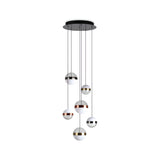 Presenting the Arionis 6 Light LED Cluster Pendant, a stylish lighting solution for an energy-efficient living space. This modern chandelier is designed with six spherical pendant lights suspended at varying lengths from a sleek circular black base. Each LED globe features a striking design, half white and half metallic, adorned with an elegant mix of gold, silver, and copper finishes.
