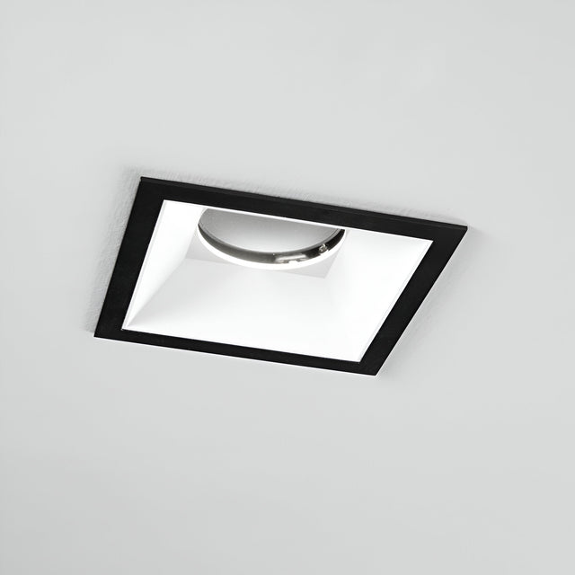 The Glistenis Trim Square Frame 106mm in black offers a modern, recessed ceiling light design with a sleek finish and reflective interior. Shown turned off against a plain white ceiling, it exemplifies the elegance of contemporary downlight installations.
