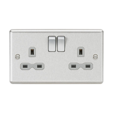 The 13A 2 Gang DP Switched Socket With Twin Earths in brushed chrome features a sophisticated design with double pole switches and two plug outlets. Its elegant appearance is enhanced by the grey insert and rounded edge, all securely fastened with two screws on each side.