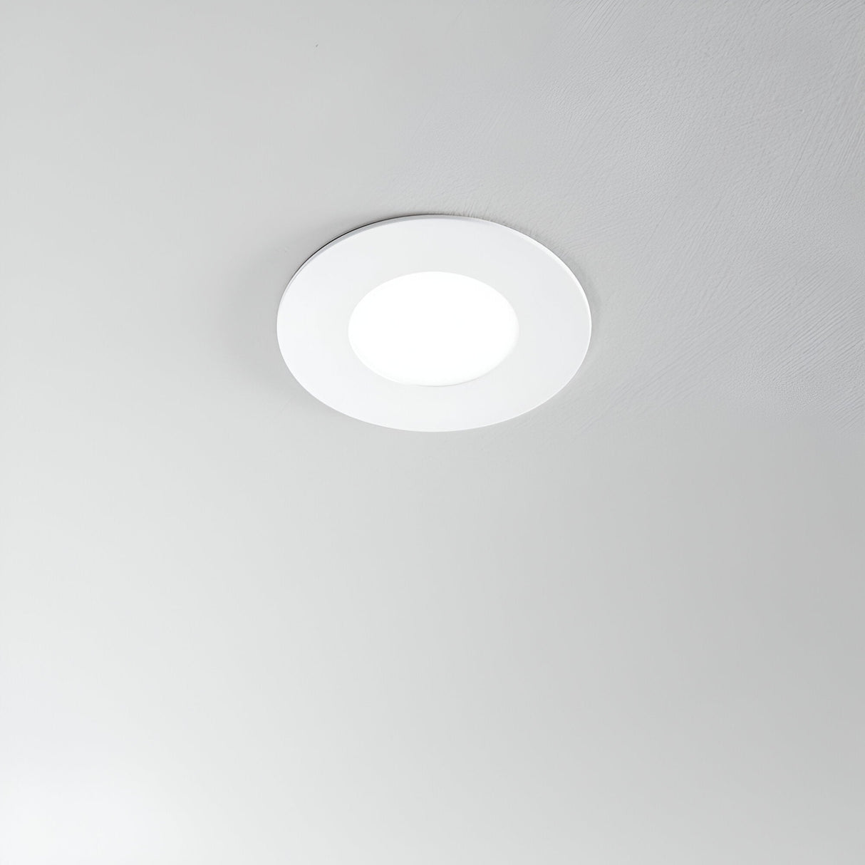 A circular Solix LED Recessed Downlight - 7W, 4000K in white emits a soft glow from the ceiling, contrasting beautifully with the smooth light gray background and highlighting its energy-efficient brilliance.