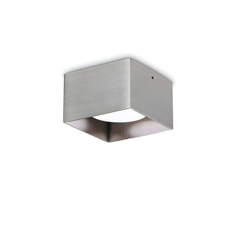 The Orbis Square Downlight - Nickel is a modern ceiling fixture with a brushed metal, square design. It features a recessed, replaceable LED light source aimed downward, offering contemporary illumination in a sleek and minimalist style.