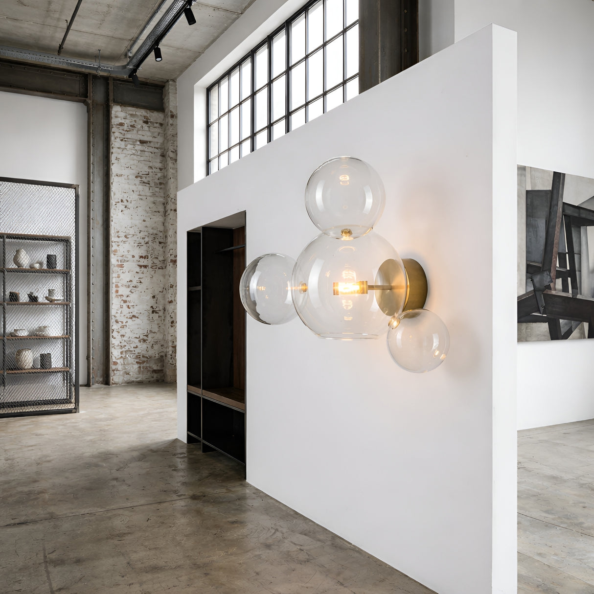 A modern industrial interior with a white partition wall features the Bubble LED Glass Wall Light - Gold, composed of clear glass globes, set against concrete floors and exposed brick walls.
