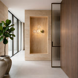 A modern, minimalist hallway with beige stone walls, a Bubble LED Glass Wall Light - Gold, large potted plant, floor-to-ceiling windows, and a wooden partition with vertical grooves is filled with natural light.