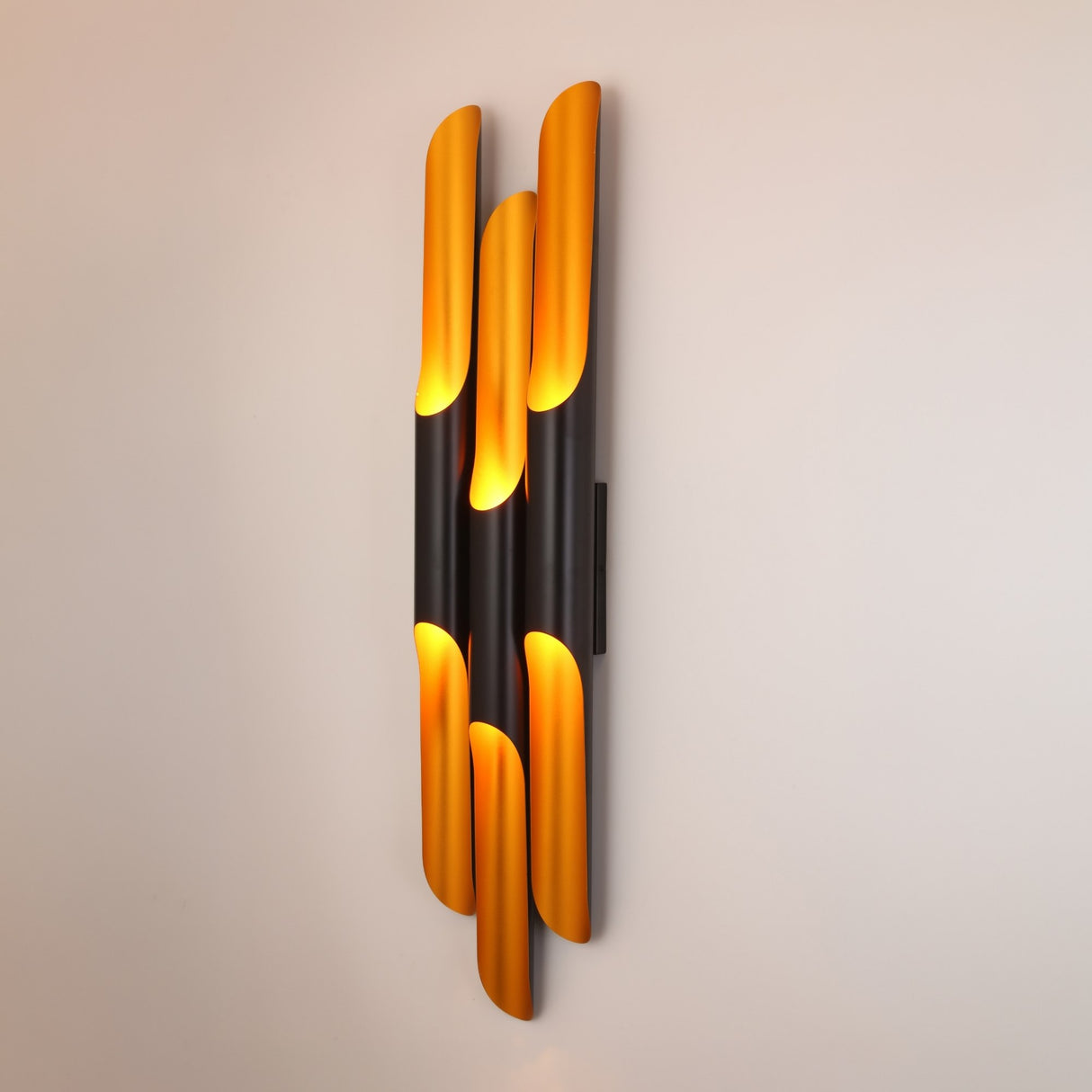 The Stealth 6 Light Wall Light in brass and black features vertically arranged cylinders that emit warm yellow light, casting a soft glow on any wall—an elegant addition to architectural wall lighting design.
