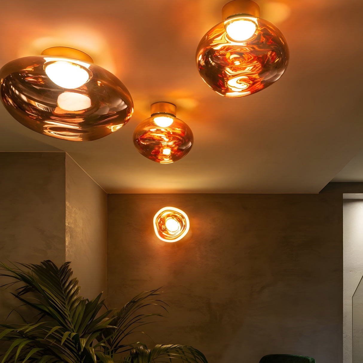 The Lava Small LED Wall & Ceiling Light in copper casts a warm glow in a stylish, minimal room with textured walls and a leafy plant—highlighting the organic elegance of modern lighting design.
