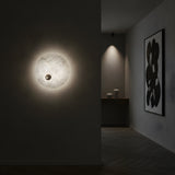 A minimalist interior features the Selvana LED Small Alabaster Wall Light - Soft White casting a gentle glow, an abstract black-and-white painting on the wall, and a console table with two vases in the background.