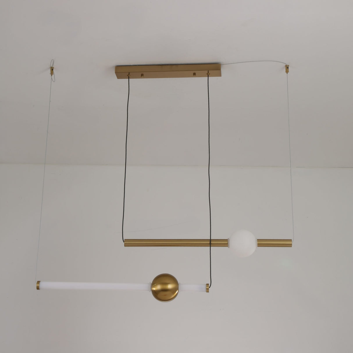 Niori Sottile LED horizontal suspension light with brushed gold linear tubes and a frosted white opal globe, shown wire-suspended from a ceiling.