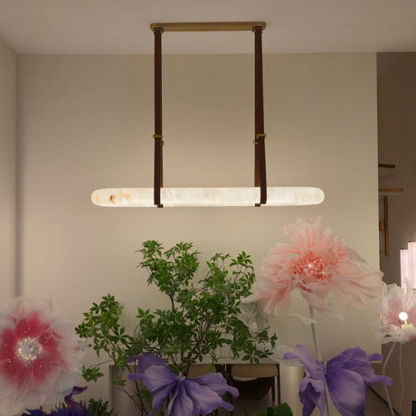 Cintura LED Medium Alabaster Oval Chandelier hangs from a copper bar by brown leather straps, glowing warm white above a room styled with flowers.